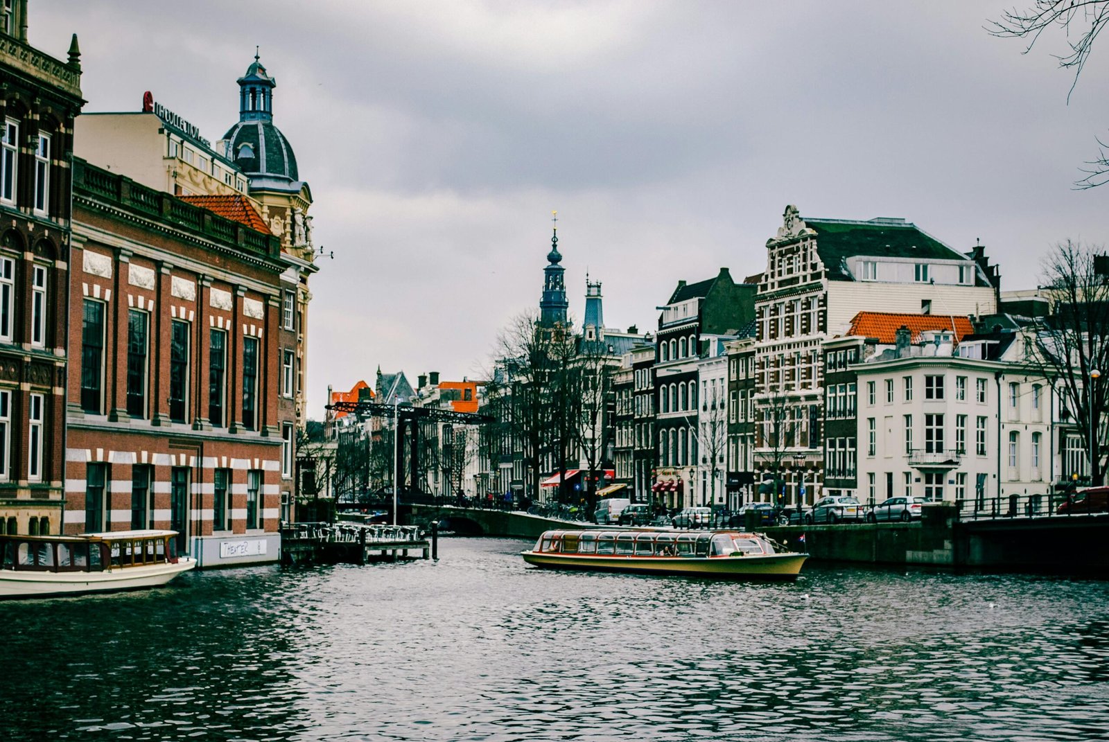 About Us Charming canal scene in Amsterdam with historic architecture and a passing boat.